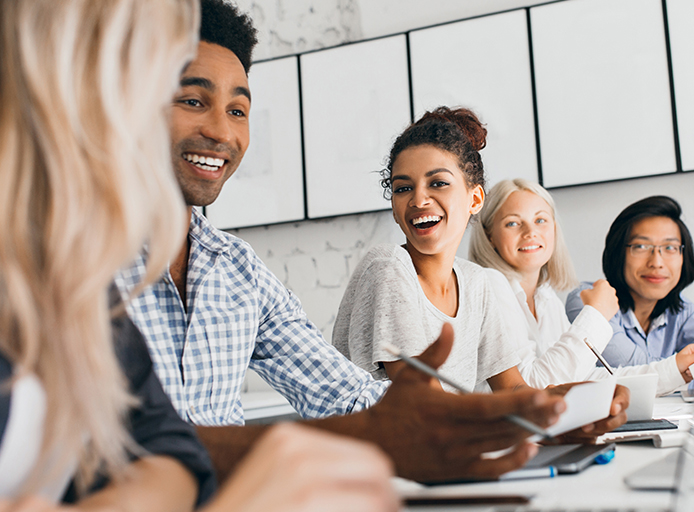 Diverse team of office workers smiling during a meeting, collaborating in a bright, modern workspace.